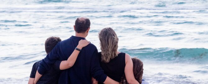 Nuclear family standing on the beach with arms wrapped around each other. Only one of many combinations in a modern relationship.